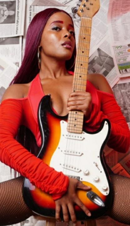 AlxZandria in red holding an electric guitar against a newsprint backdrop